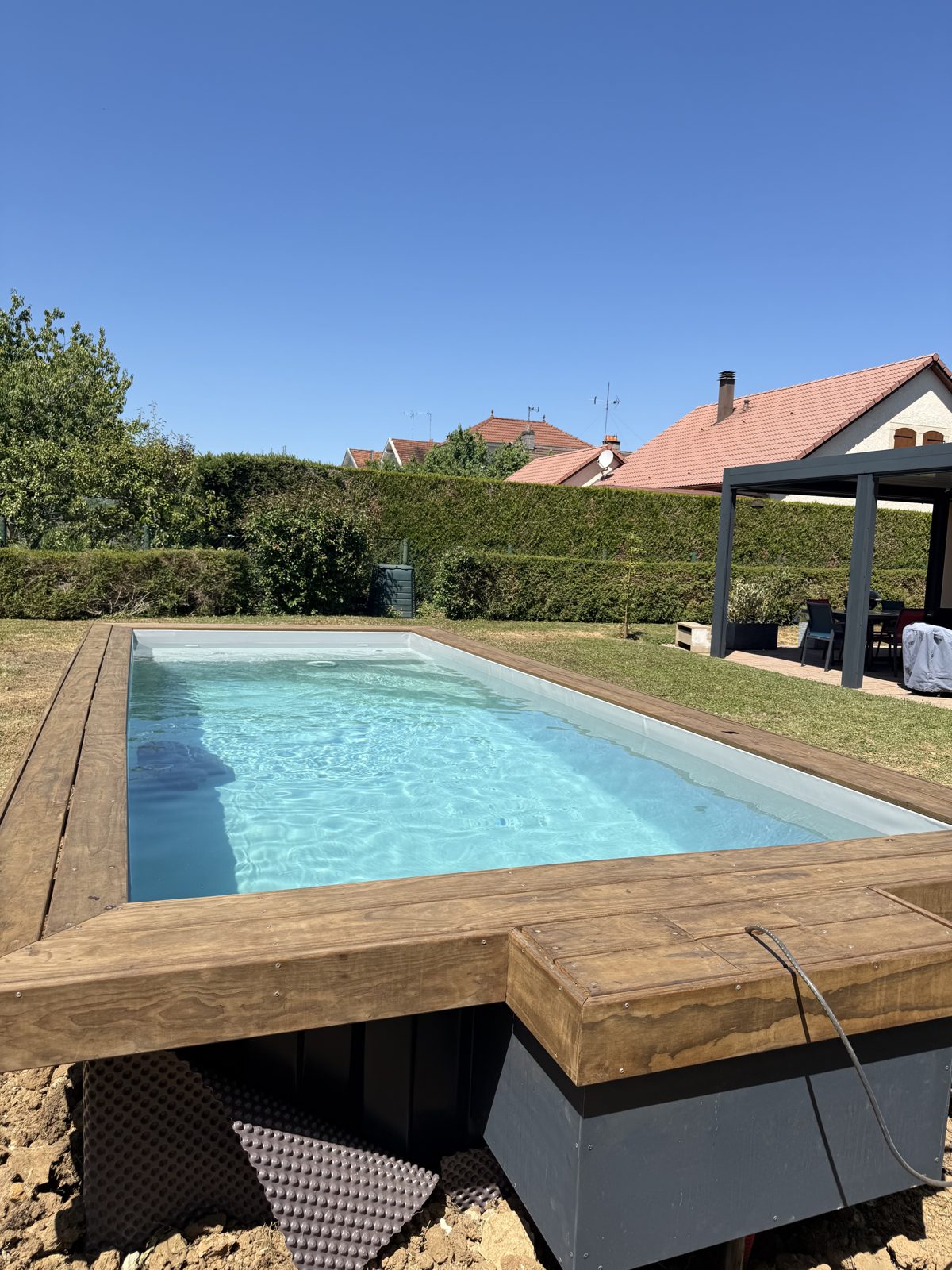 Piscine container semi-enterrée en acier avec margelle bois installée à Mirecourt dans les Vosges